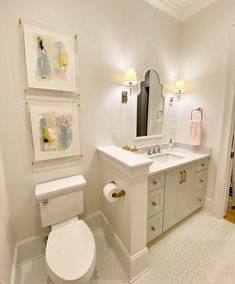 a bathroom with a toilet, sink, mirror and pictures on the wall above it