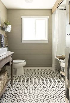 a white toilet sitting next to a sink in a bathroom under a window on top of a tiled floor