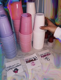 there are many different colored cups on the table and one is pointing at them with a finger