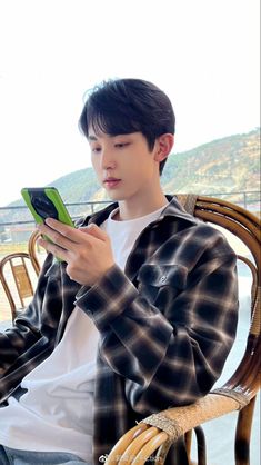 a young man sitting in a chair holding a cell phone and looking at the screen