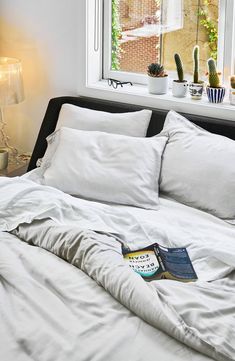 an unmade bed in front of a window with white sheets and pillows on it