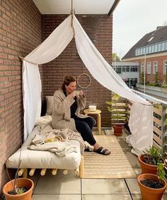 a woman sitting on top of a bed next to potted plants