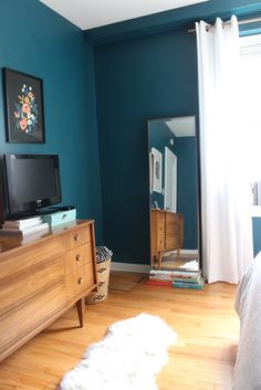 a bedroom with teal walls and wooden furniture in front of a large flat screen tv