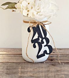 a white flower in a mason jar on a wooden table with a tag tied around it