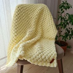 a yellow knitted blanket sitting on top of a chair next to a potted plant