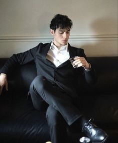 a man in a tuxedo sitting on a couch holding a drink and looking at his cell phone