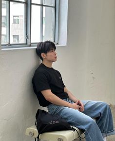 a young man sitting on top of a white chair next to a window in an empty room