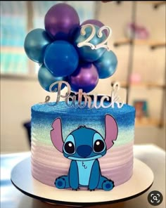 a blue and purple birthday cake with an elephant on it's top, surrounded by balloons