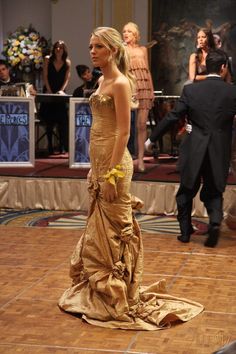 a woman in a gold dress standing on a dance floor with other people behind her