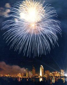 fireworks are lit up in the night sky over water and city buildings with lights on them