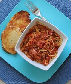 a blue plate topped with pasta and bread next to a fork on top of a blue place mat