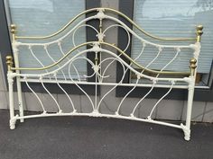 a white metal bed frame with gold colored headboard and foot board in front of a window