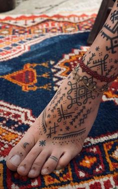 a person with tattoos on their feet and foot sitting on top of a colorful rug