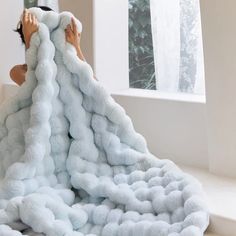 a woman laying on top of a pile of fluffy white blankets next to a window