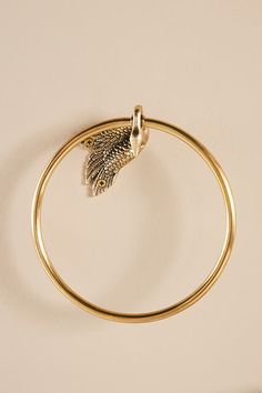 a gold bang bracelet with a leaf charm on the end and a ring around it