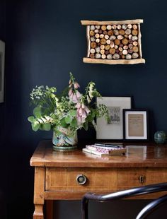 a wooden desk topped with a vase filled with flowers next to a wall mounted art piece