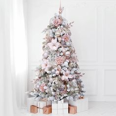 a white christmas tree with pink and silver ornaments on it, surrounded by gift boxes