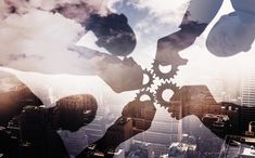 two hands holding gears in front of a cityscape with skyscrapers and clouds