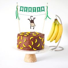 monkey cake topper with name banner and a monkey hanging from its tail over a chocolate cake with banana candy decorations Monkey Themed First Birthday, Monkey See Monkey Two Birthday Party, Monkey 1st Birthday Boy, Monkey Cake Ideas, Monkey See Monkey Two Birthday, Monkey Theme Cake, Monkey Cake Topper, Birthday Cake Banner, Monkey Party Ideas