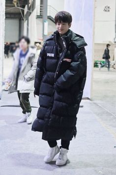 a young man is walking down the street wearing a black coat and white sneakers, with his hands in his pockets