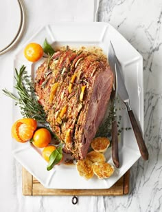 a large piece of meat sitting on top of a white plate next to oranges