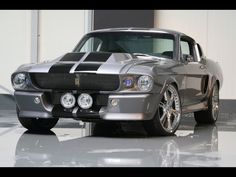 a silver muscle car with black stripes on it's hood and front end, parked in a garage