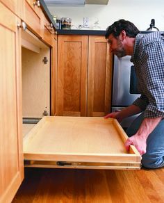 a man kneeling down in front of an open drawer on the kitchen counter top,