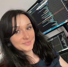 a woman sitting in front of a computer monitor with lots of data on the wall behind her