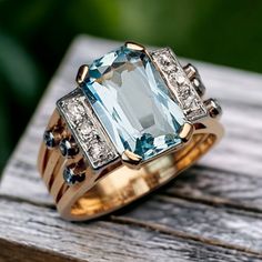 two gold rings with an aqua blue topazte surrounded by diamonds on a wooden surface