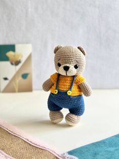 a small crocheted teddy bear wearing overalls and a yellow t - shirt