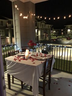 the table is set for two on the balcony at night with rose petals all over it