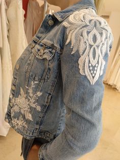 a woman wearing a jean jacket with an embroidered design on it