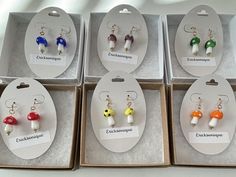 six pairs of earrings are displayed in their boxes on the table with each individual's name