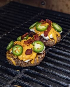 two hamburgers covered in cheese and jalapenos on top of a grill