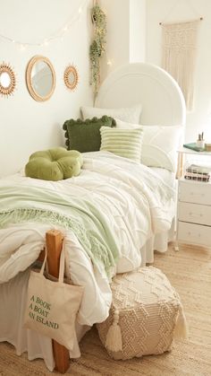 a white bed with green pillows and blankets on it's headboard in a bedroom