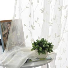 a table with a potted plant on top of it next to a white curtain