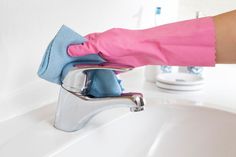 a person in pink gloves is cleaning a white sink with a blue towel and rag