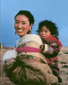 a woman carrying a child on her back in an open area with grass and blue sky