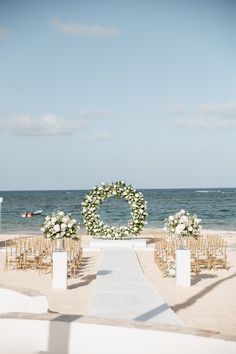 an outdoor ceremony set up on the beach with white flowers and greenery in front of the ocean