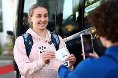 a woman is smiling and holding something in her hand while standing next to a bus