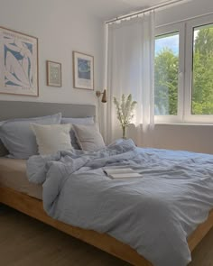 a bed with blue sheets and pillows in a bedroom next to a large window on the wall