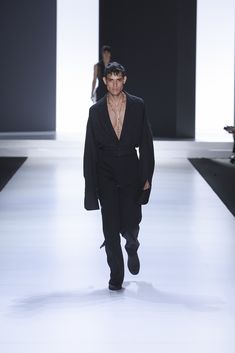 a man walking down a runway in a black suit