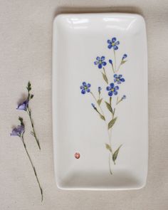 a white plate with blue flowers on it next to a small purple flower that is in the center