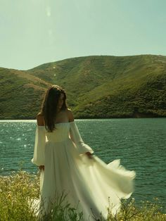 a woman in a white dress is standing by the water and looking off into the distance