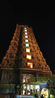 a very tall building with many lights on it's sides and people walking around