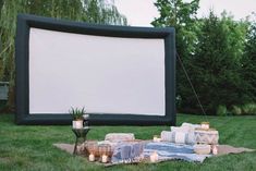 an outdoor movie screen is set up with candles and blankets on the grass in front of it