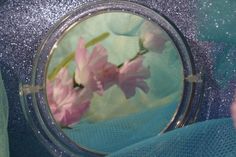 a close up of a mirror with pink flowers in front of it and a person's hand holding the mirror