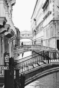 a black and white photo of a bridge over a canal in venice, italy with people walking on it