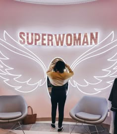 a woman standing in front of a sign that says superwoman with wings on it