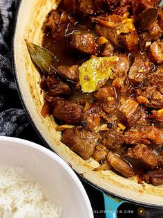 a pan filled with meat and rice on top of a blue table cloth next to a white bowl